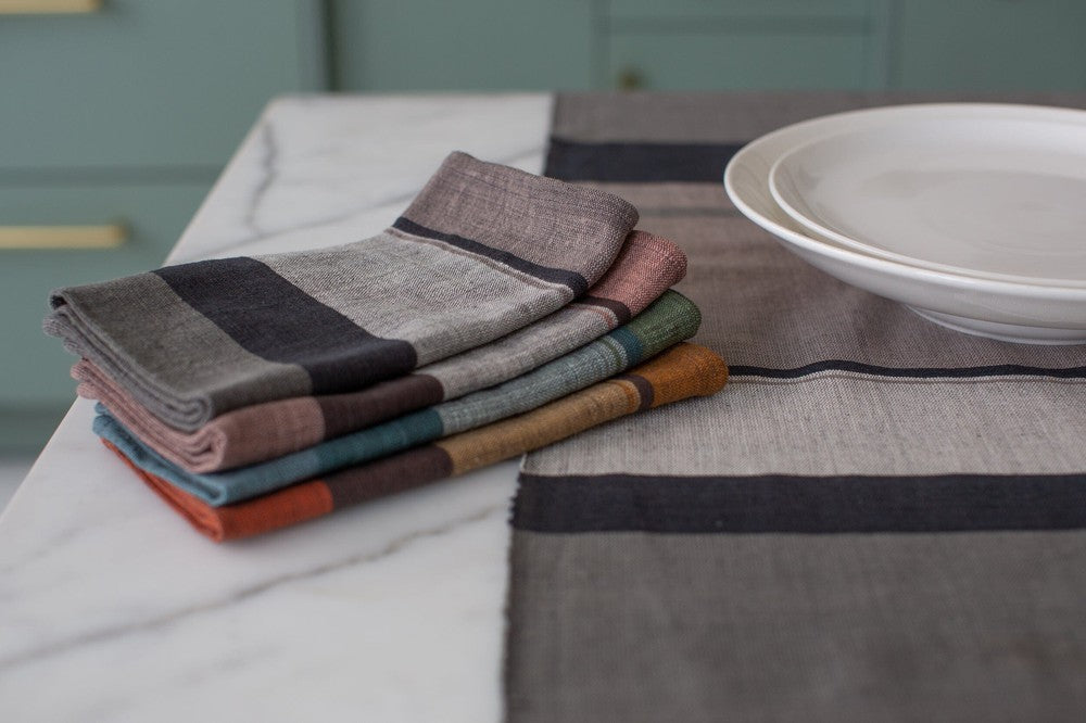 Stack of color block cotton napkins on a kitchen counter beside white plates and a table runner