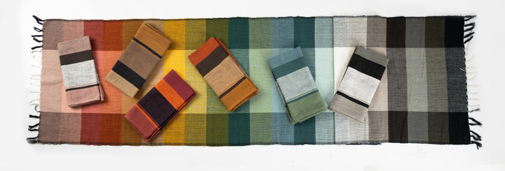 Six folded color block napkins laid along a striped handwoven table runner