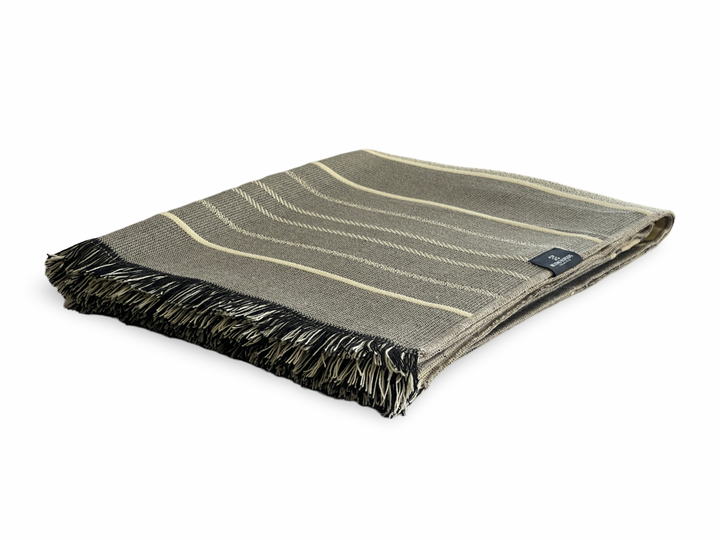 Equinoccio fringed throw in cream, grey, soft brown, and black banding, folded to show the tasseled edge.