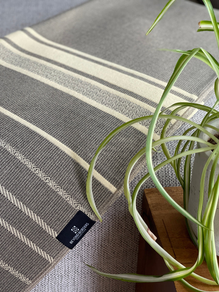 Handwoven Equinoccio Cedar Brown throw in cream with grey and brown bands.