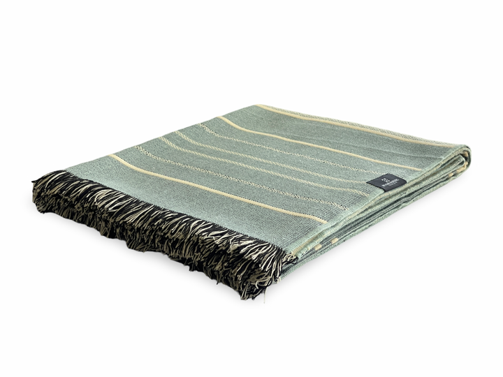 Equinoccio fringed throw in cream, dusty mint, and sage-blue banding, folded to show the tasseled edge.
