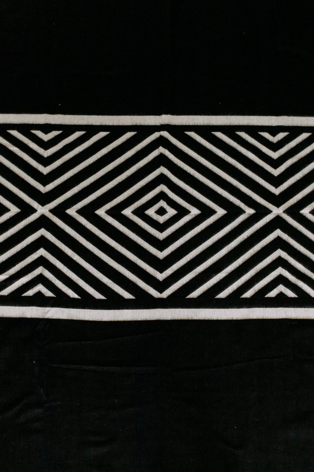 Paramo Andean blanket in black and cream with a bold concentric diamond geometric, draped around a person outdoors.