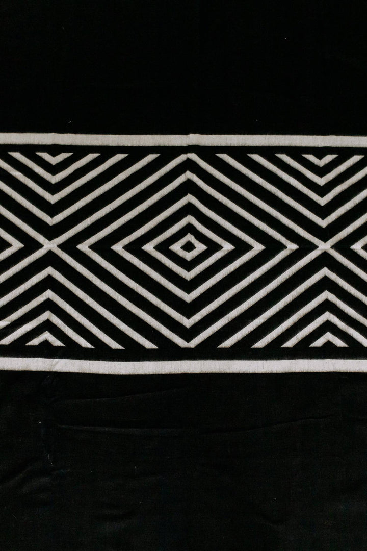 Paramo Andean blanket in black and cream with a bold concentric diamond geometric, draped around a person outdoors.