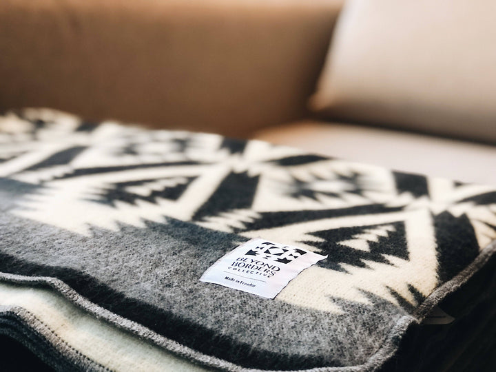 Handwoven Andean throw blanket in black and charcoal on cream, draped outdoors.
