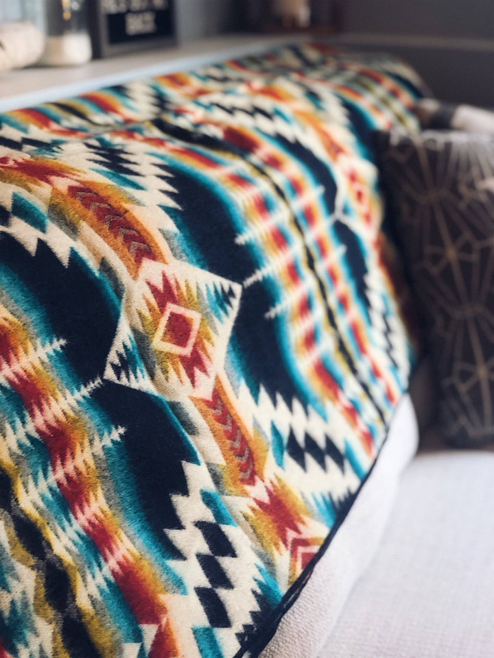 Northern Lights Andean throw blanket with a navy-bound edge.