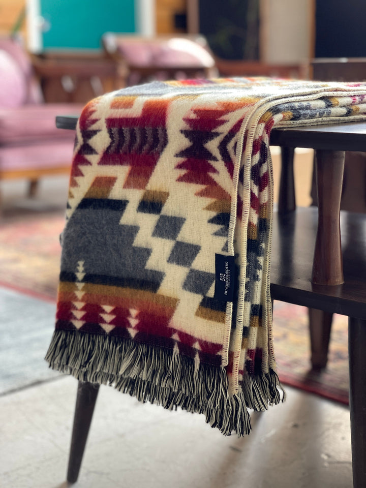 Campfire Ash Andean throw draped on a sofa, showing the tasseled fringe edge.