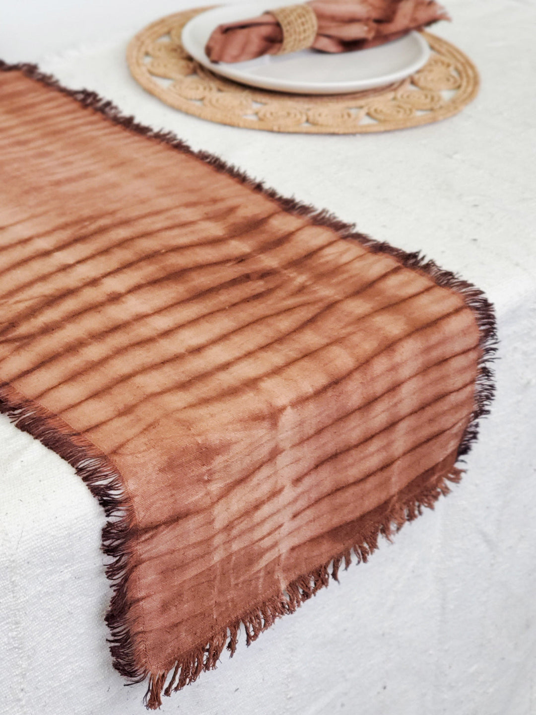 Hand-dyed shibori cotton table runner in warm rust and cream with fringed edges