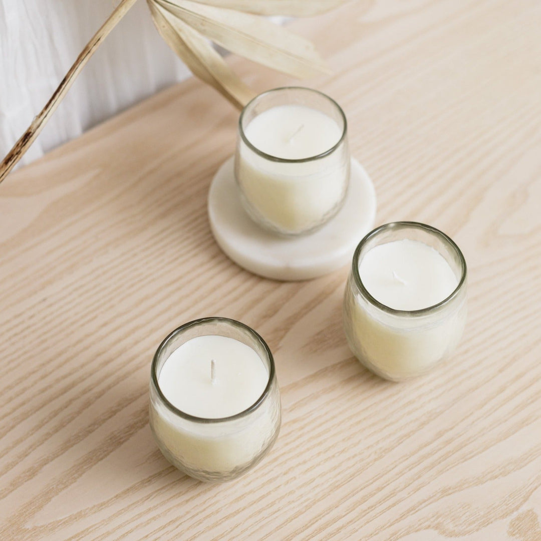 Set of three soy wax votive candles in textured hammered-glass vessels.