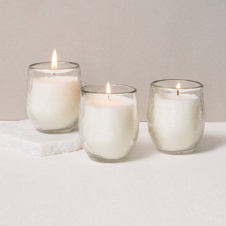 Three hand-poured soy votive candles casting warm light through hammered glass.