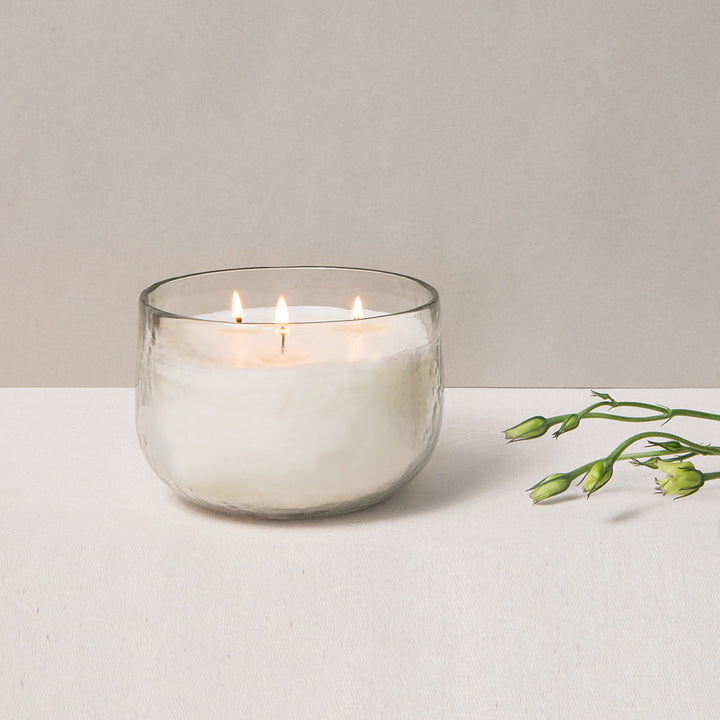 Hand-blown glass triple-wick soy candle bowl illuminated from within.
