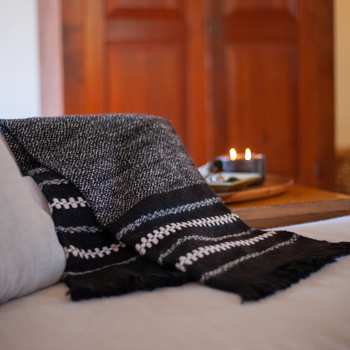 Black alpaca throw blanket with cream and grey stripes draped on a bed