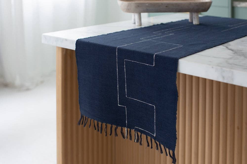 A navy cotton table runner hanging over the edge of a marble counter with fringe at the end.
