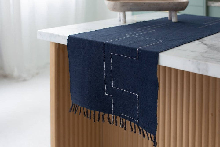 A navy cotton table runner hanging over the edge of a marble counter with fringe at the end.