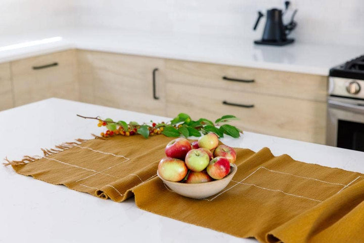 An ochre cotton table runner on a kitchen island with a bowl of apples and a berry branch.