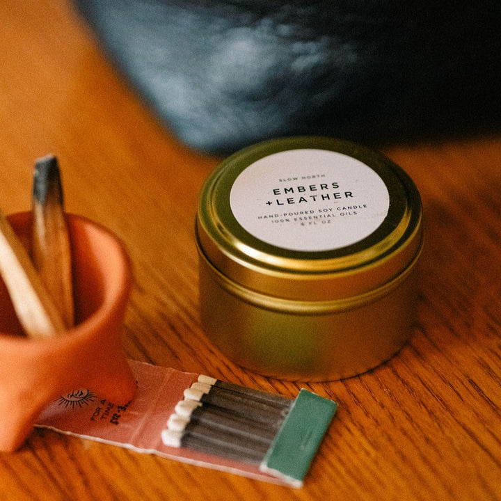 Embers &amp; Leather candle in a 6 oz brushed gold tin with vetiver, cedar, and patchouli scent.