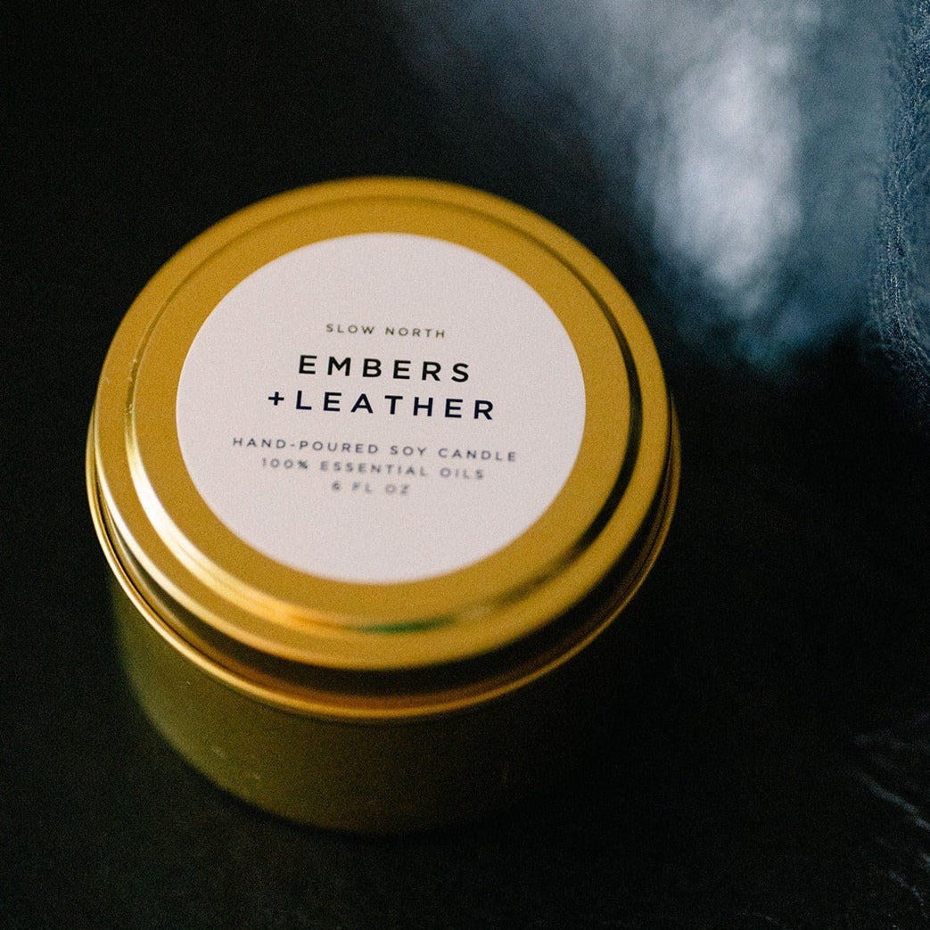 Embers &amp; Leather soy candle in a brushed gold travel tin with warm vetiver, cedar, and patchouli notes.