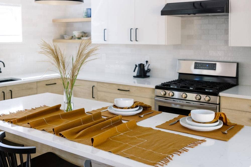 Woven cotton table linens in ochre set along a white kitchen island with bowls and napkins.