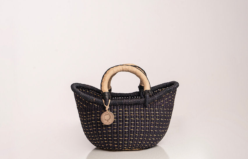 The Petite Victoria handwoven straw basket bag with a leather handle and intricate weave.