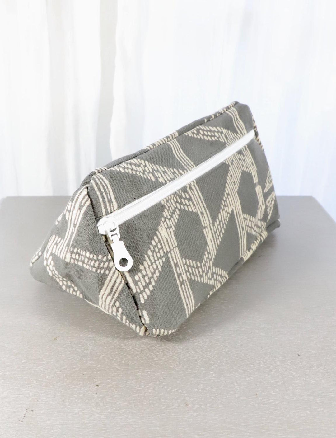 Grey cotton toiletry bag with a triangle or floral pattern and zip closure.
