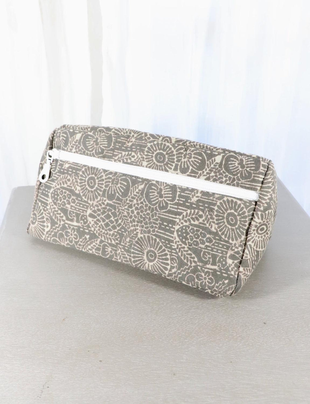 Grey cotton toiletry bag with a triangle or floral pattern and zipper closure.