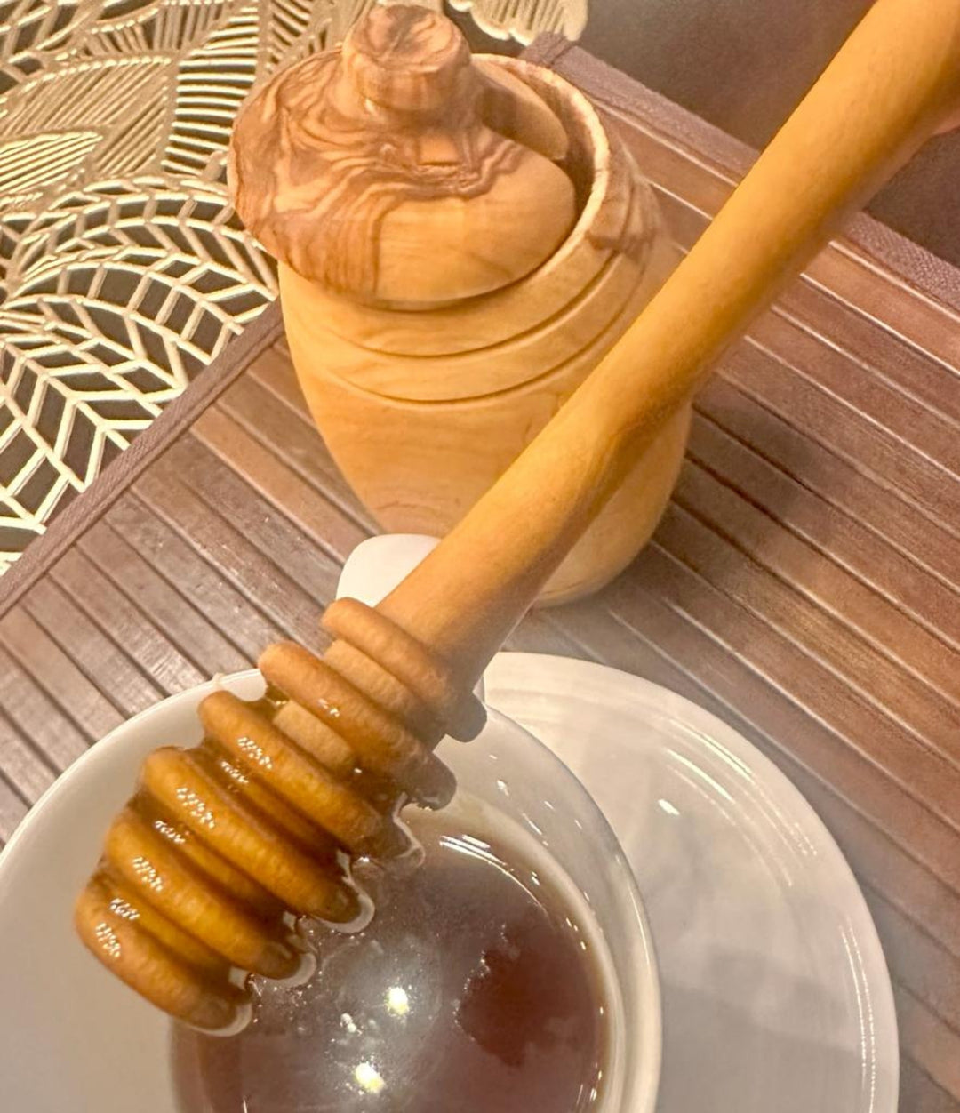 Olive wood honey spoon resting on a honey pot, showcasing natural wood grain and Mediterranean craftsmanship.