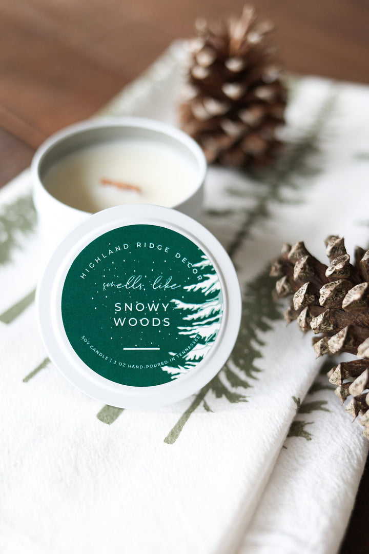 Snowy Woods soy candle in a tin with a wooden wick and winter-forest label.