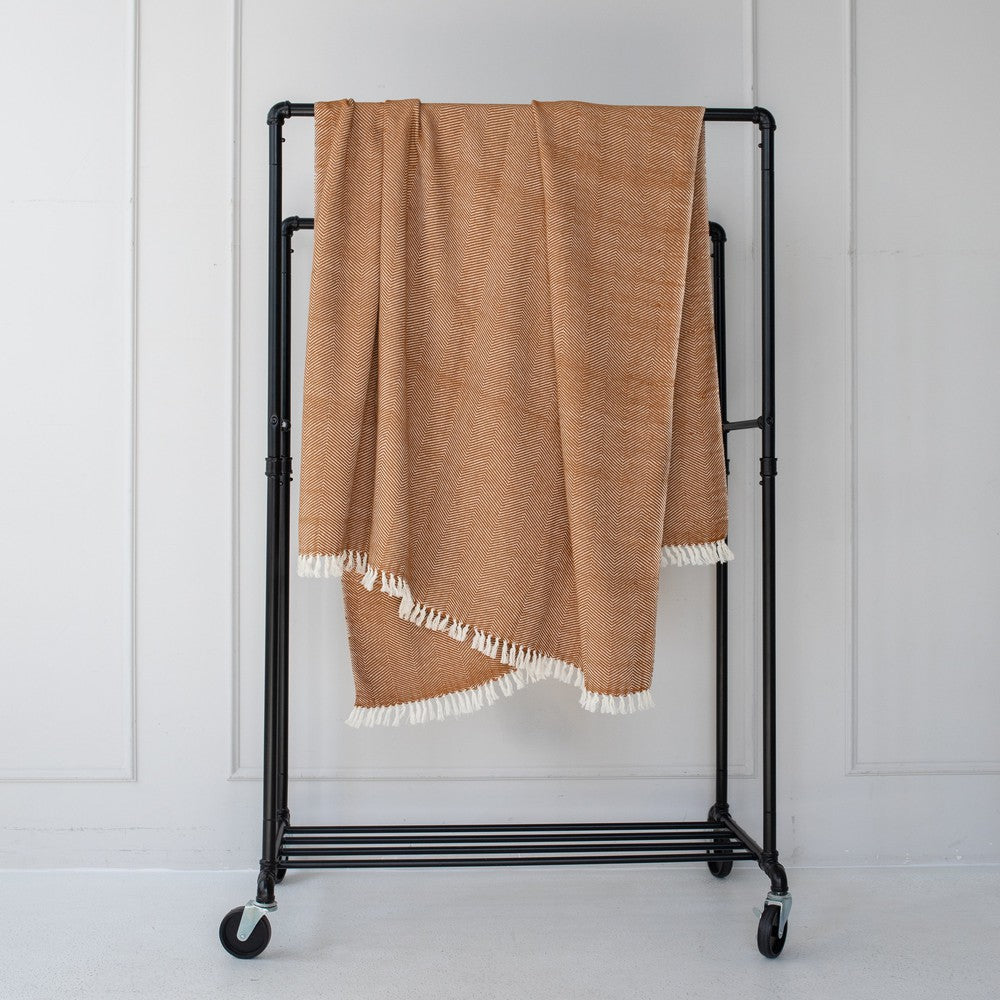Bronze herringbone cotton throw hanging on a black clothes rail against a white wall, with natural white fringe.