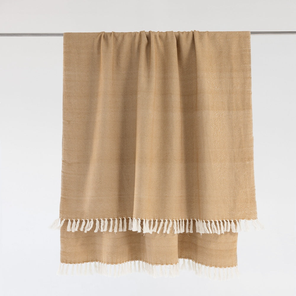 Almond herringbone cotton throw hanging from a rail, with natural white fringe.