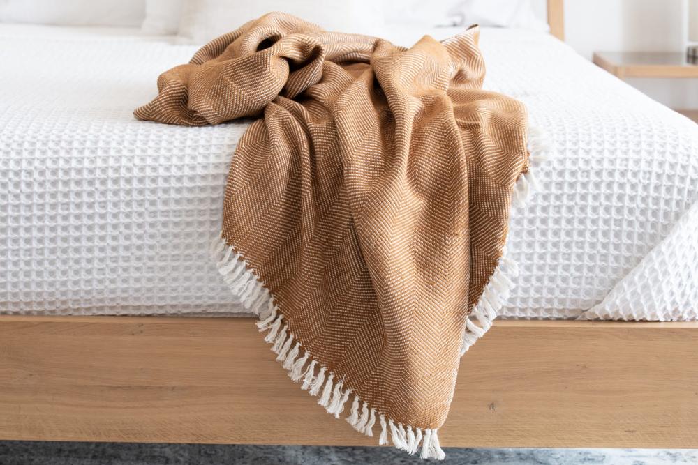 Bronze herringbone cotton throw tossed over the foot of a bed with white waffle bedding.