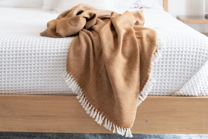 Bronze herringbone cotton throw tossed over the foot of a bed with white waffle bedding.