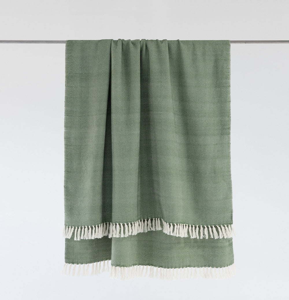 Mint herringbone cotton throw hanging from a rail, with natural white fringe.