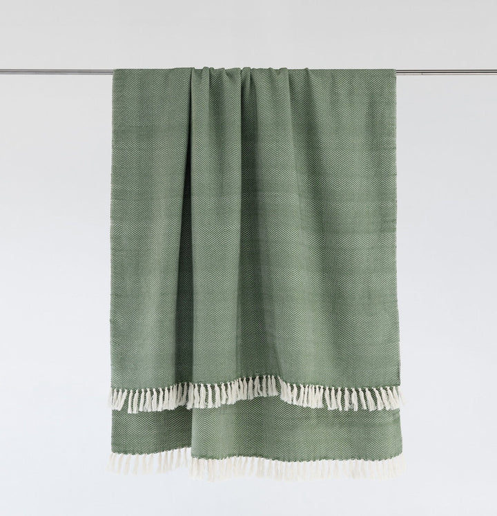 Mint herringbone cotton throw hanging from a rail, with natural white fringe.