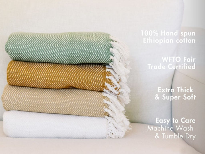 Stack of folded herringbone cotton throws with notes: 100% hand-spun Ethiopian cotton, WFTO Fair Trade certified, extra thick and soft, machine wash and tumble dry.