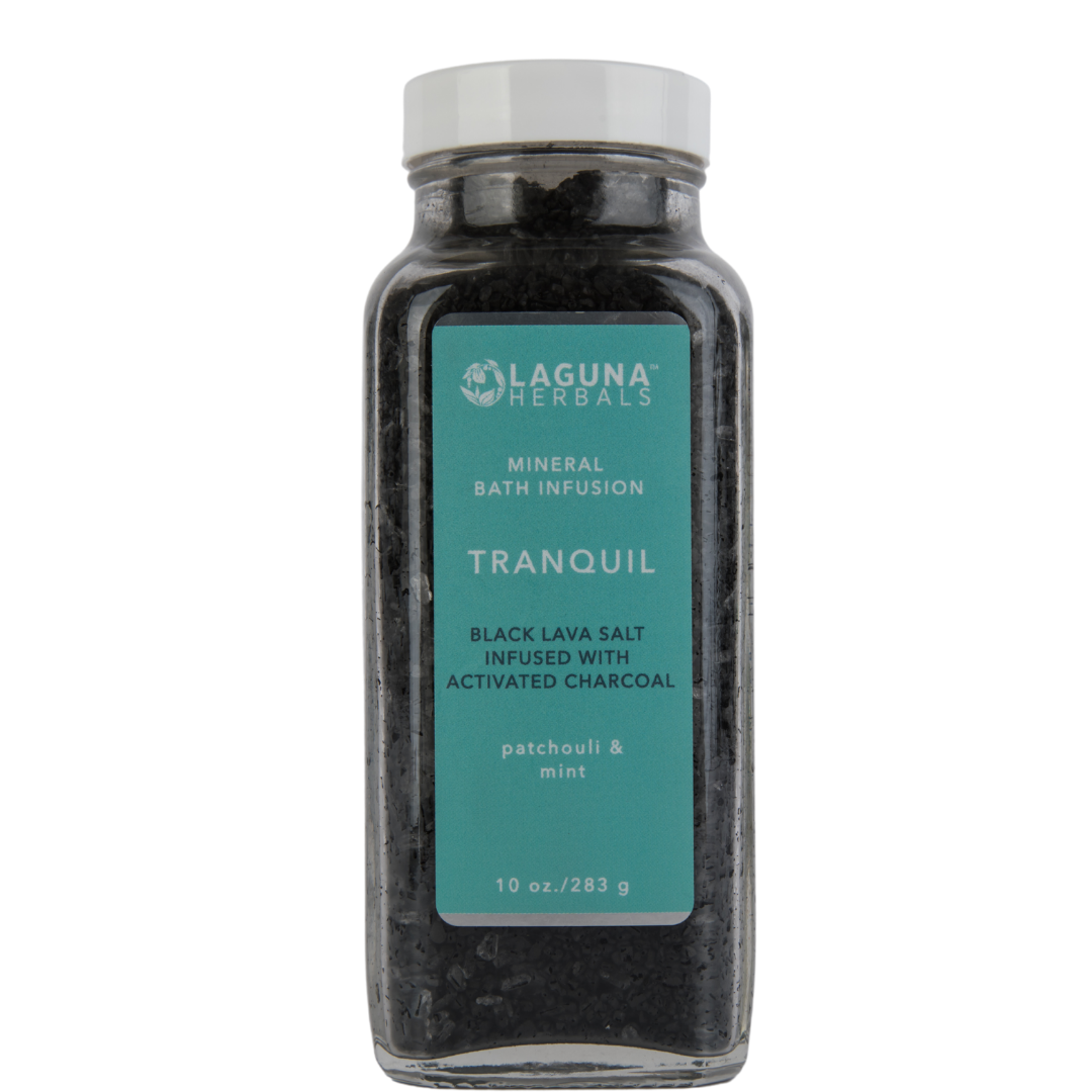Black lava bath salt with activated charcoal in a glass jar, with a wooden scoop.