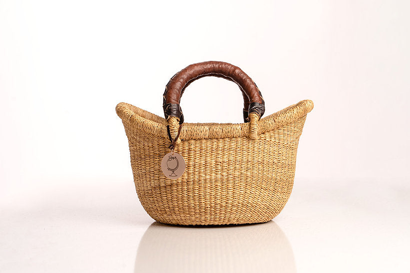 The Petite Victoria handwoven straw basket bag with a leather handle.
