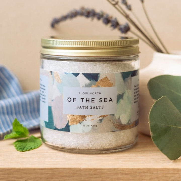 Clear glass jar of Of The Sea bath salts with mineral salt crystals visible.