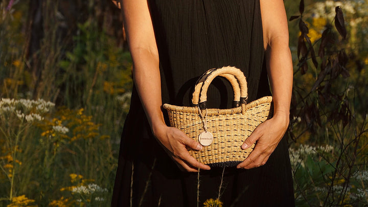 The Petite Victoria handwoven straw basket bag with a leather handle and natural woven design.