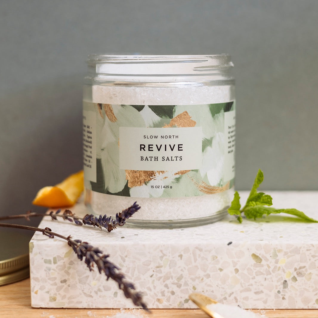 Glass jar of Revive bath salts with colorful mineral salts visible through clear packaging.