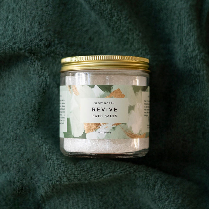 Clear glass jar of pink-toned bath salts on a neutral background.