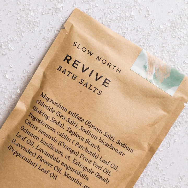 Kraft pouch of Revive bath salts with essential oil blend and visible colorful salt crystals.