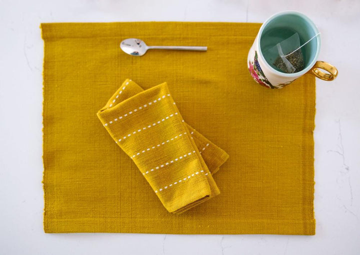 Gold cocktail napkin folded on a matching placemat with a teacup