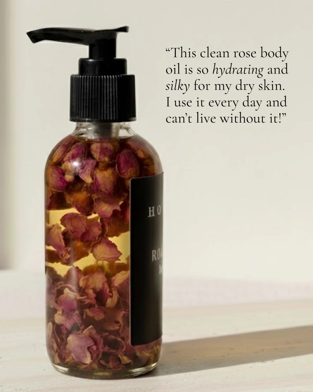 Organic rose body oil in a clear glass bottle with a dropper and fresh roses.