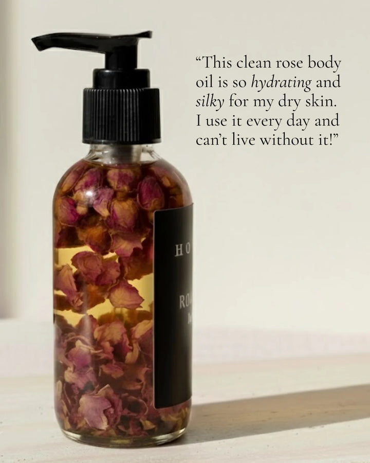 Organic rose body oil in a clear glass bottle with a dropper and fresh roses.