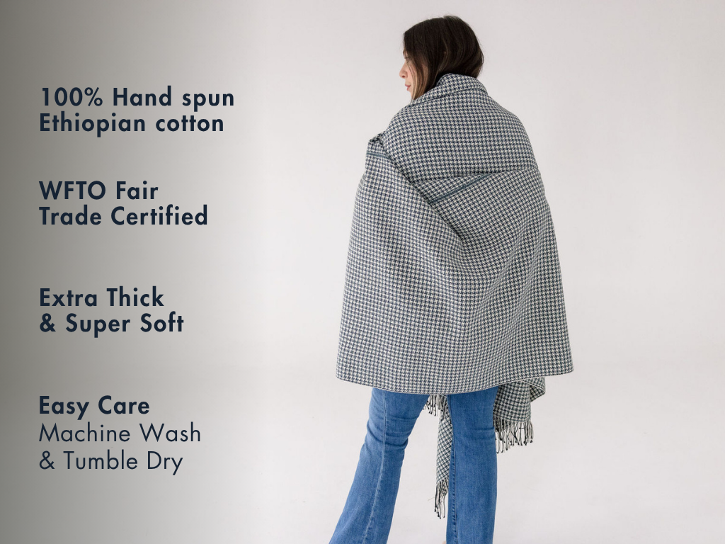 Slate pinwheel cotton throw wrapped around a person, with notes: 100% hand-spun Ethiopian cotton, WFTO Fair Trade certified, extra thick and soft, machine wash and tumble dry.