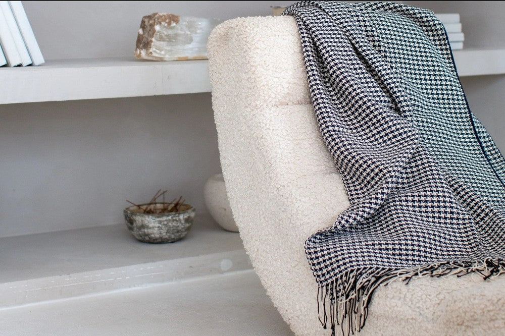 Slate pinwheel cotton throw draped over a cream boucle lounge chair beside built-in shelves.
