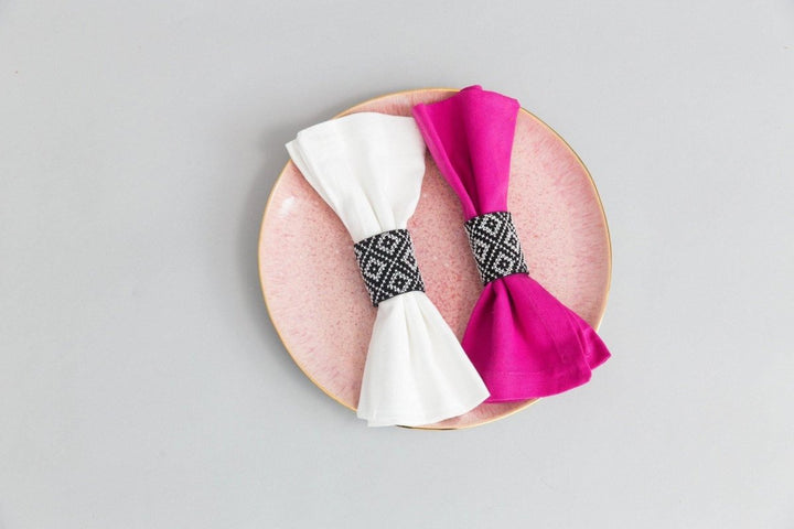 Set of two black napkin rings with white geometric tatreez cross-stitch and brass snaps.