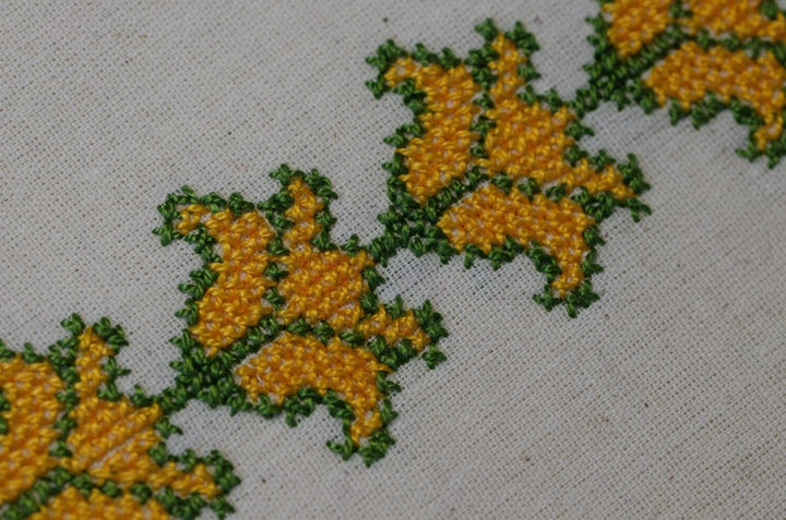 Folded hand-embroidered Cauliflower tatreez tea towel in yellow and green.