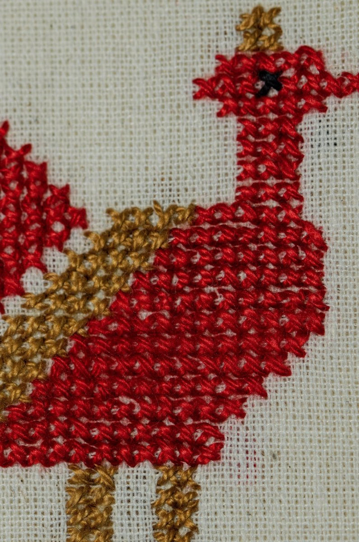Close-up of the red and tan Rooster tatreez embroidery on natural cotton.