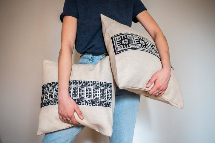 Black-and-white Moon with Feathers motif hand cross-stitched on a natural oatmeal cushion cover.