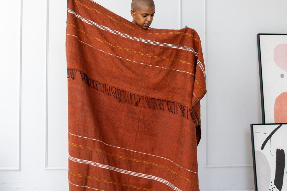 Person holding the copper cotton throw open against a white wall.